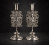 <p>Par de castiçais de prata-de-lei regional sem contraste, finamente cinzelados, ornamentados com figura feminina semi-desnuda e símbolos de colheita, ramagens e guirlandas, placa apoiada sobre base de madeira nobre. Alt. 35 x 13 x 13cm. América do Sul, séc. XVIII (peso total com madeira 1.590 gramas)</p>