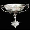 Fruteira/Centro de mesa em metal prateado. Pé com figura de putino e bacia com frutos em relevo. Mede 32 cm de altura e 27 cm de diâmetro . Possui desgastes do tempo como mostra a foto.
