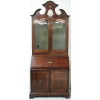 Bookcase em madeira, com frisos em metal dourado, com influência inglesa, com 2 bandas de porta inferiores, sob gabinete com tampo reclinável, tendo no seu interior 4 gavetinhas e 1 portinha. Parte superior com 2 bandas de portas com vidros estando estas sob 2 gavetas. Apresenta no ápice pequeno espelho incrustado na madeira. Guarnições em bronze. Med. 230x95x48cm. 