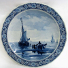 H. W. Mesoluq - Belo medalhão, do Séc. XIX, em porcelana de Delft - Joost Thoopt a Labouchere, com pintura ao centro de marinha com figuras e barcos, nos tons de azul em degrade. Assinado. Aba com flores. Diam. 30cm. 