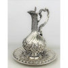 Belo claret jug com presentoir em prata contrastada, teor 833 milésimos, com trabalhos em gomos curvos, flores, folhas e volutas. Alt. claret jug 31,5cm e Diam. presentoir 28,5cm. Peso 2.030g. 