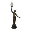 Grande luminária de chão em petit bronze representando Jovem sustentando tocha com vestes patinadas de dourado. Cúpula em vidro com trabalhos em forma de chamas de fogo. Alt. 160cm.