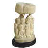 Parte de grosso bloco de presa de marfim africano esculpido com representação de figuras sob uma proteção. Base de madeira. Alt. total 25cm. 