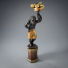 BLACKAMOOR VENEZIANO <br />ESCULTURA EM MADEIRA ENTALHADA, CARNADA E POLICROMADA.<br />MENINO ESCRAVO, SEGURANDO CORNUCÓPIA COM FRUTAS (Símbolo de fartura).<br />BASE SEXTAVADA, ARRANJO DE FRUTAS EM METAL DOURADO REBATIDO A MÃO.<br />ITÁLIA, SÉCULO XIX.<br />MEDIDAS da peça: 105cm x 47cm x 35cm.<br />MEDIDAS da base: 44cm x 32cm x 32cm. <br /><br />Entre os séculos XVII e XVIII, figuras em madeira laqueadas e douradas aparecem no mobiliário veneziano, como prateleiras, pedestais, porta-vasos.<br /><br />A figura do servidor que sustenta tampos, vasos, almofadas é muitas vezes a do Moro, personagem desde o século XVI ligado à imagem de Veneza.<br /><br />O Moro, portanto, já aparece no gabinete que Vittore Carpaccio pintou, em 1490, para a família Moncenigo e também apareceu nas grandes telas da Última Ceia e das Bodas de Caná pintadas pelos Mestres Venezianos da século seguinte.<br /><br />Eram representados, no século XVIII vestidos à moda oriental, ou com ricos mantos de seda entrelaçados com ouro, com ricos saiotes e cocares imaginativos. Assim encantando a moda, ordenado uma tradição que há muito foi usada.
