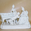 Wolfgang Amadeus MOZART (1756-1791). Grupo escultórico figurando o menino Mozart tocando para realeza. Grupo em porcelana bisquit vidrada. Consta apenas de numeração baixo relevo. <br />Origem alemã ou Austríaca, século XIX. <br />Peso: 1.578 g. Medidas: 20 x 26 x 16 cm.