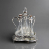 <p>Servi&ccedil;o de tr&ecirc;s licoreiros em bandeja de metal com banho de prata. Base em de galeria vazada figurando parras. Garrafas no estilo Claret com al&ccedil;a e tampo articulado. Bojo em cristal lapidado &agrave; m&atilde;o figurando parras. Importado. Medidas: 34x24x24 cm.</p>