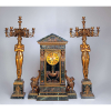 Conjunto de grande relógio de mesa de mármore e par de candelabros de bronze. O relógio em forma de pórtico ao estilo império, ornamentado nas laterais por leões alados e na parte frontal par de cariátides, com finíssimos ornamentos de bronze dourado, mostrador circular e pêndulo em forma de naveta. Os candelabros com figura feminina à guisa de fuste, sobre base pedestal de mármore encimada por sete braços recurvos, 67 x 27 x 90 cm de altura, o relógio, 115 cm de altura (cada candelabro). França, séc. XIX.