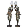 <p>Casal de Black-a-moors de Madeira. Veneza, século XIX/XX. Casal de black-a-moors de madeira entalhada e policromada com temas orientalistas em relevo sobre cobertura ebanizada. Cada um dos personagens porta elaborado turbante sobre a cabeça presos por fieiras de pérolas entrelaçadas. Trajam botas e, à maneira de ligas, elementos dourados rematados por simulacro de cabochons. No pescoço elaborados colares em relevo com pingentes em forma de gotas. Uma das mãos segura pequeno plateau e, a outra erguida, cornucópia eletrificada em meados do séc. XX e acendedor em porcelana. Parte superior da cornucópia da figura masculina apresenta restauro antigo; 135 cm e 136 cm de alturas totais. Acompanham duas cúpulas de cristal Baccarat, uma delas com pequena perda na borda.</p>