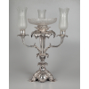 Exuberante centro de mesa e candelabro de prata indo-inglesa. Corpo ricamente adornado com profusão de elementos fitomórficos. Apresenta na base reserva com as seguintes inscrições: Presented to F. C. Sandes C S Q re by Prince Aftaboodeen Great Grand Son of Tipoo Sultan 1851. Parte superior finalizada com três mangas e uma fruteira de cristal lapidado e fosqueado. Apresenta contraste e marcas de prateiro – Alt. 70 cm – Inglaterra Séc. XIX<br />