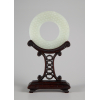 Disco de Jade Branco (BI) -A pedra branca, esculpida em ambos os lados em baixo relevo com um padrão denso de espirais em forma de vírgula entre bandas sulcadas na borda e no centro sobre um suporte de madeira entalhada - Diâm. 7 cm - China, C.1794 - Dinastia Qing, período Qianlong.<br />
